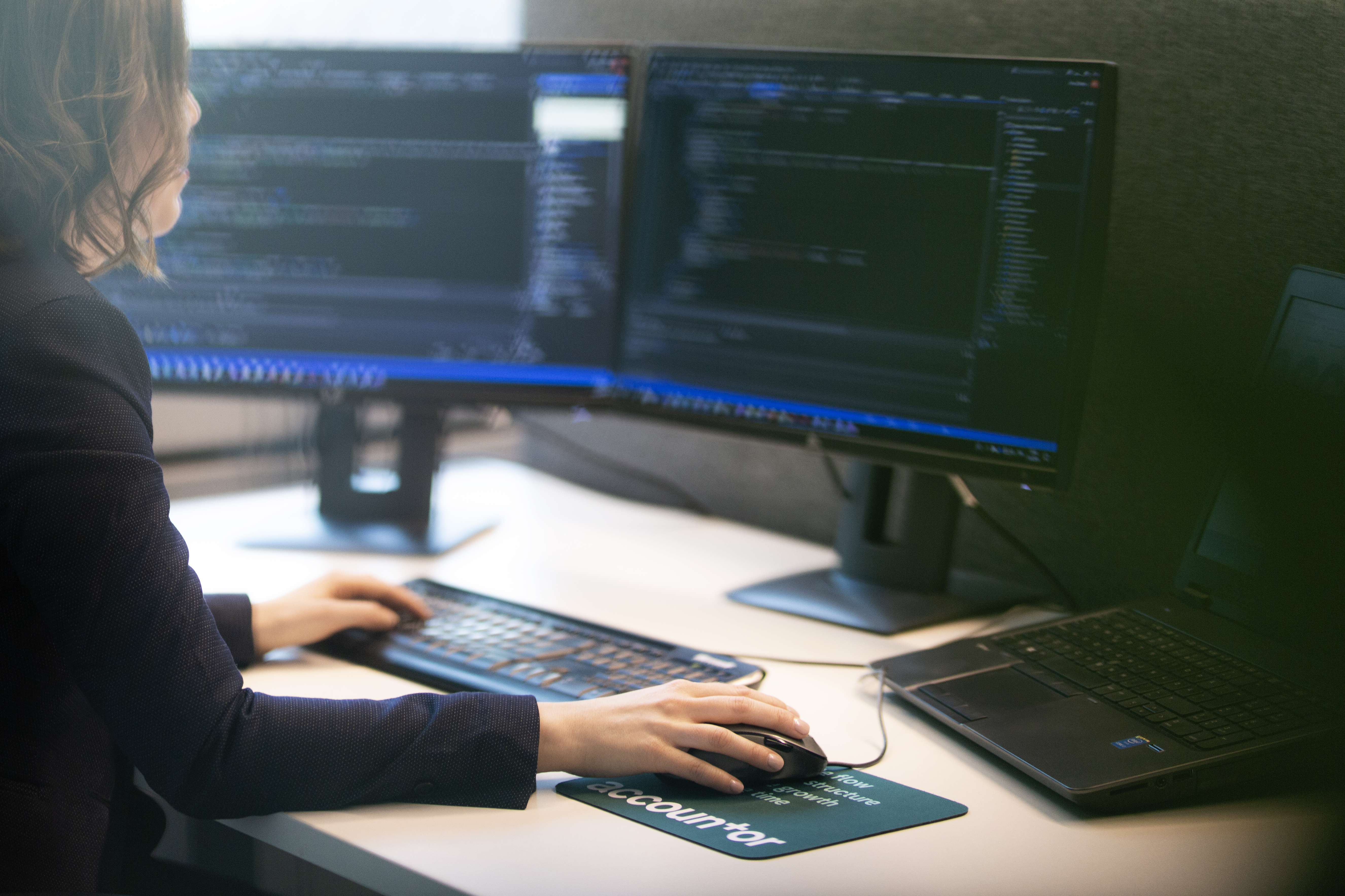Kvinne som sitter foran en pc med masse koding på skjermen