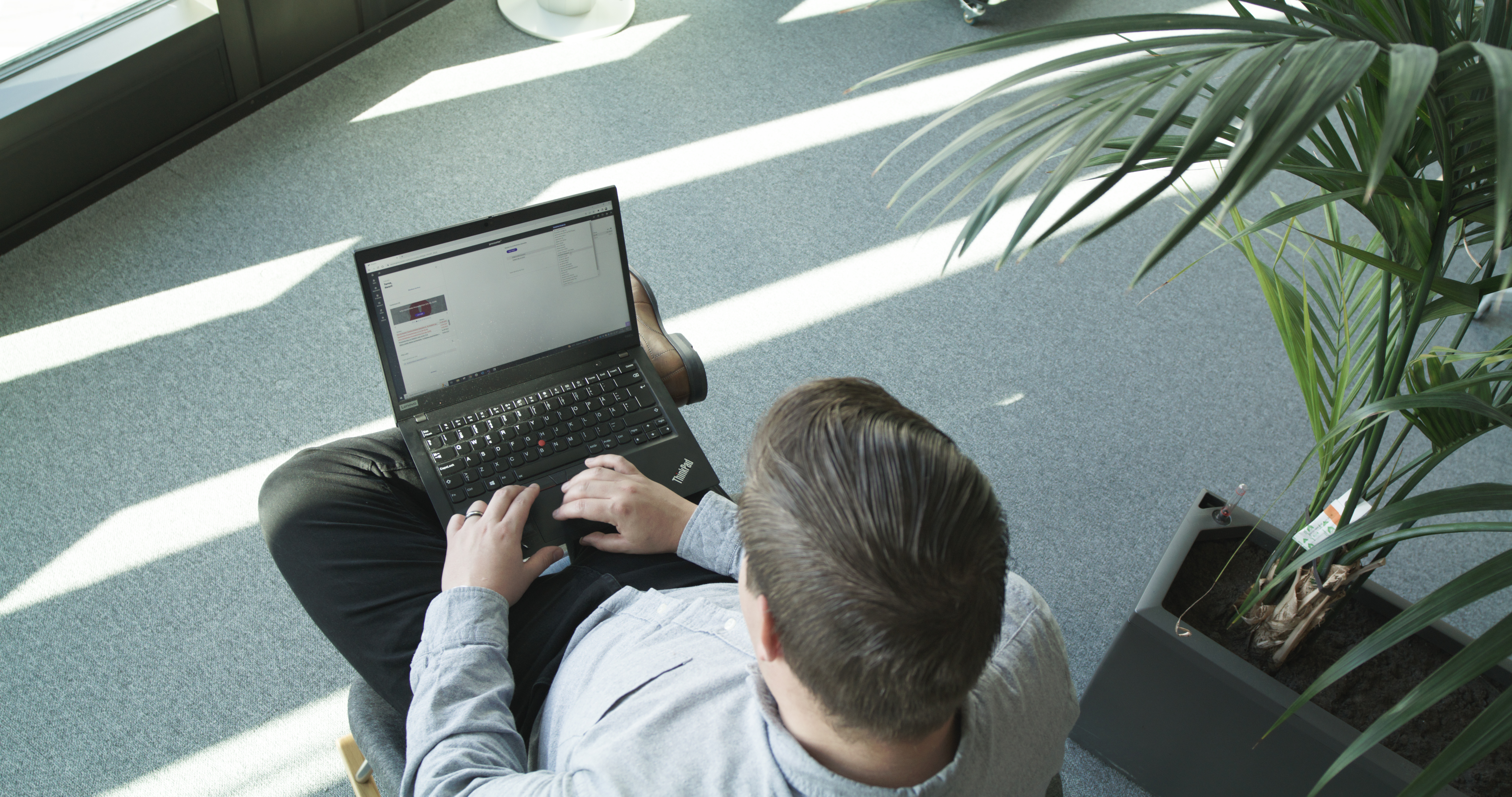 Mann med laptop  sitter i en stol med planter rundt