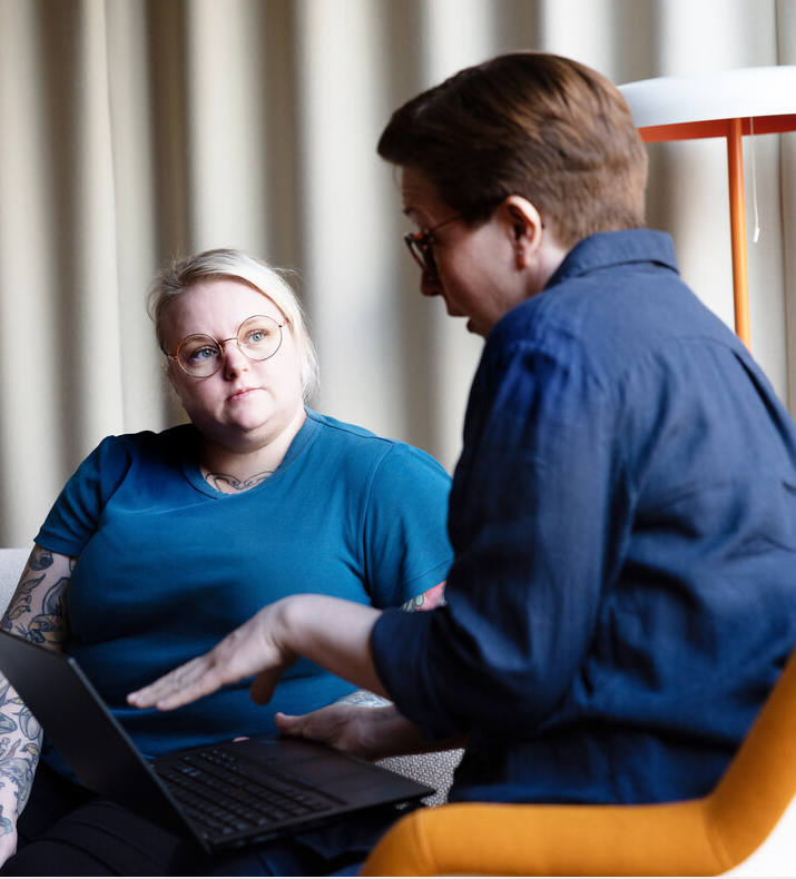 to kvinnelige kolleger som sitter å snakker i en sofa med en laptop i mellom