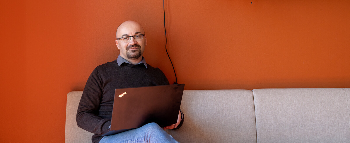 Timo i en sofa med pc. hvit sofa mot rødoransje vegg