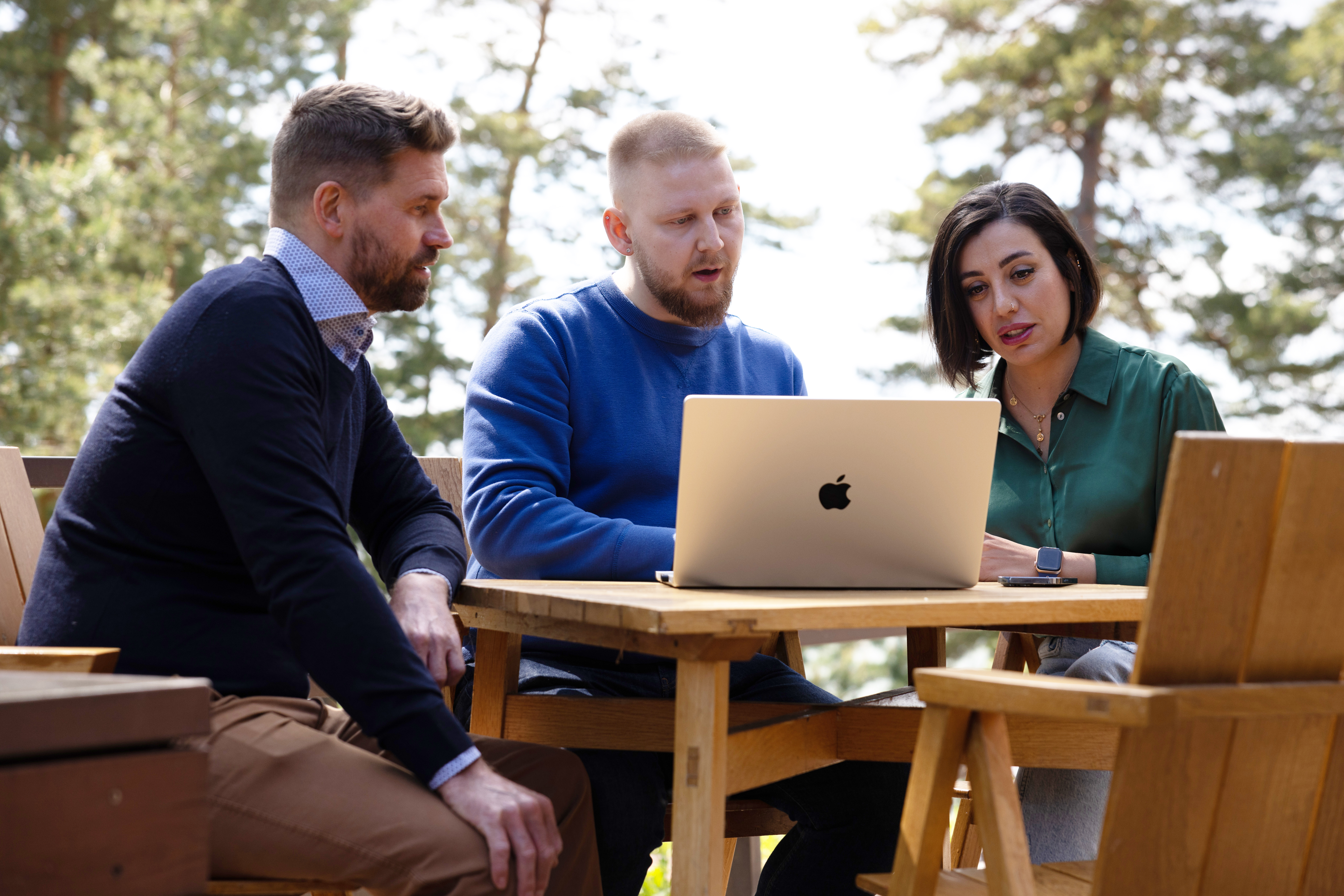tre kollegaer som sitter sammen foran en mac og diskuterer innholdet i fint sommervær.