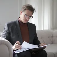 Mann i en sofa som sitter tenkede og reviderer et dokument